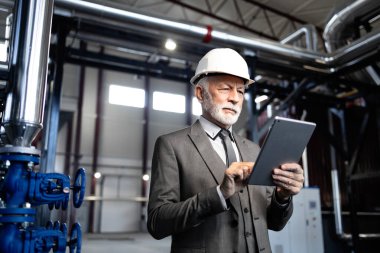 İşletme sanayi sisteminde tabletle kıdemli işadamı, fabrika operasyonlarını denetliyor.