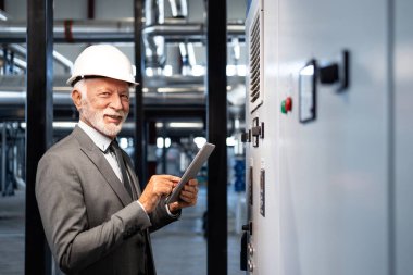 Tabletli, kasklı kıdemli işadamı endüstriyel tesis operasyonlarını izliyor.