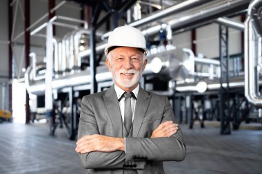 Rafineride kollarını kavuşturmuş kasklı, gülümseyen olgun bir yönetici.