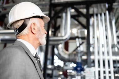 Üst düzey işadamı, modern petrokimya tesisi operasyonlarını izleyen bir şapka takıyor.