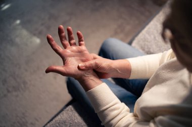 Yaşlı kadın bilek eklem iltihabından dolayı acı çeken eline masaj yapıyor. Rahatsızlık duyuyor ve eklemleri ağrıyor.