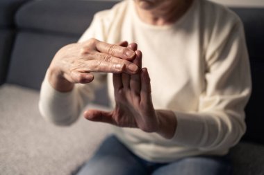 Yaşlı bir kadın eklem ağrısı ve eklem iltihabı yüzünden elleri kanepede dinleniyor.