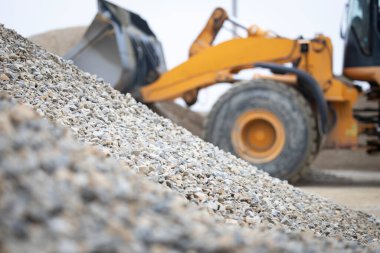 Sarı tekerlek yükleyici kova, bulutlu gökyüzünün altındaki endüstriyel bir inşaat sahasında ezilmiş çakıl kepçesi, güçlü toprak taşıma ekipmanları, altyapı işleri için birikim yapıyor.