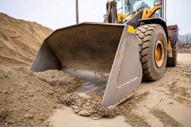 Tekerlek yükleme kovası kum ve çakıl topluyor, inşaat alanında ağır işler yapıyor, makinelerin toprak taşıma ve geliştirme projelerindeki rolünü gösteriyor