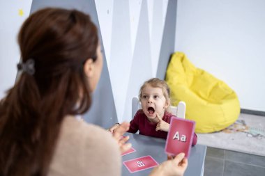 Konuşma terapisti çocuğun telaffuz ve konuşma terapisi çalışmalarına yardım ediyor, dil edinme üzerine odaklı destekleyici bir oturum sırasında alfabe bellek kartı tutuyor