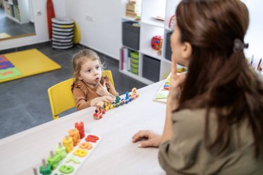 Genç bir kızla çalışan konuşma terapisti, dil gelişimi ve sözlü motor becerilere odaklanan, özel bir terapi seansı sırasında eğitim amaçlı oyun aktiviteleri ve iletişim egzersizleri kullanan