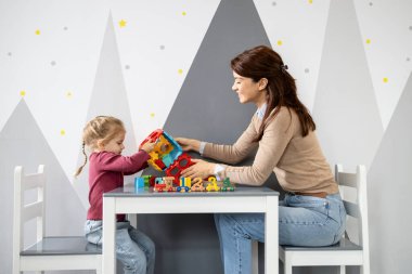 Anaokulu öğretmeni, küçük bir masada otururken, bir şekil ayırıcı ve ahşap numara treniyle oynamasına yardım ederek, erken çocukluk ortamında bilişsel becerileri teşvik ediyor.