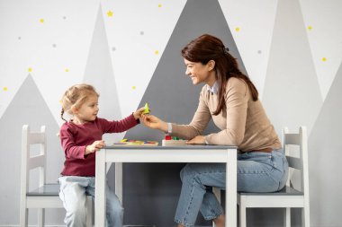 Öğretmen ve genç kız bir öğrenme aktivitesine girişiyor. Küçük bir masada geometrik şekillerle ve eğitici oyuncaklarla oynamak. Bir sınıf ortamında erken eğitim ve gelişimi teşvik etmek