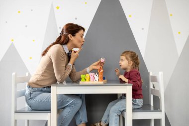 Konuşma terapisti, konuşma sorunları olan genç bir kıza yardım ediyor. Rahat bir çocuk odası ortamında konuşma egzersizleri ve iletişim becerileri üzerinde çalışıyorum. Erken dil gelişimine odaklanmış