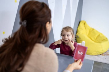 Konuşma terapisti genç kıza konuşma egzersizinde yardım ediyor, bilgi kartlarıyla bir dil oturumu yapıyor, konuşma ve iletişim becerilerini geliştiriyor, çocuk terapisi kavramı