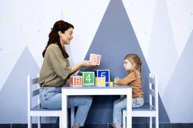 Çocuk psikoloğu, öğrenmeyi, bilişsel gelişmeyi ve eğitimsel oyunu kolaylaştırmak için renkli sayı ve harf blokları kullanarak bir terapi seansında bir anaokulu kızıyla ilişki kuruyor.