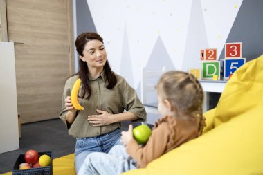 Konuşma terapisti, iletişim geliştirme dersi sırasında bir çocukla iletişim kuruyor, meyve oyuncaklarını ses pratiği yapmak ve destekleyici bir ortamda dil gelişimini arttırmak için kullanıyor.