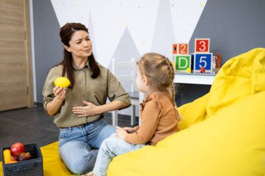 Konuşma terapisti, bir klinik ortamında yüz ifadelerini ve konuşma eklemlerini uyarmak için bir limon kullanarak gelişim terapisi sırasında küçük bir çocukla etkileşime geçiyor.
