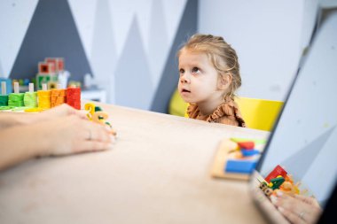 Anaokulu öğretmeninin elleri, renkli bir sınıfta bir çocuğa rehberlik ediyor, bilişsel gelişim ve beceri geliştirme için ahşap oyuncaklarla erken eğitim aktivitelerine katılıyor.