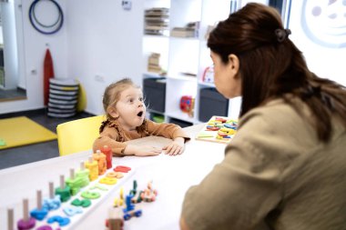 Genç bir çocuk, özel bir erken gelişim oturumu sırasında eğitici oyuncaklar kullanan bir kadın konuşma terapistiyle çene ve dil konuşması yapıyor.