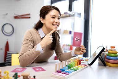 Konuşma terapisti bir öğrenciyle çevrimiçi bir ders veriyor, eğitim ve konuşma gelişimi için bir teleoterapi oturumu sırasında C harfi ile telaffuz ediyor.