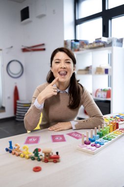 Konuşma terapisti, konuşma gelişimini, konuşma eklemlerini ve erken müdahale becerilerini desteklemek için eğitim oyuncakları ve kartlarla gülümseyen ve dil ve sözlü motor egzersizleri sergiliyor.