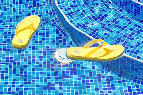 Par de chinelos em uma piscina azul — Fotografia de Stock