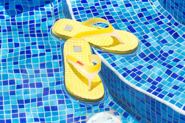 Par de chinelos em uma piscina azul — Fotografia de Stock