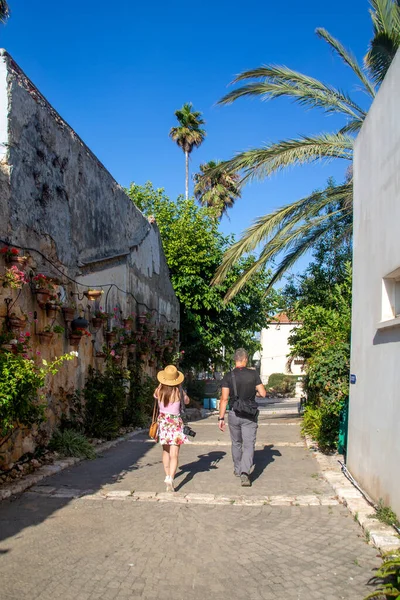 Young woman and man walking down the street by the wall of hanging plant pots with flowers and irrigation systemat the Midrechov Street in Zichron Yaakov Israel