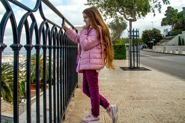 teenage girl in a lilac jacket against the background of the city of haifa, the Bahai Garden