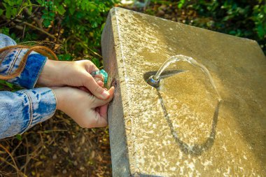 Çocukların elleri sıcakta su içmek için dışarıdaki çeşmenin düğmesine basıyor.