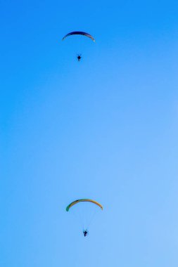 Mavi gökyüzündeki paragliderler havadan akrobasi yapıyorlar. Havada spor var. 