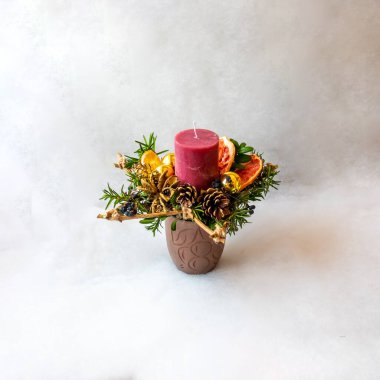 kozalaklı dallarla, kozalaklarla ve kurutulmuş portakal dilimleriyle süslenmiş kırmızı mum.