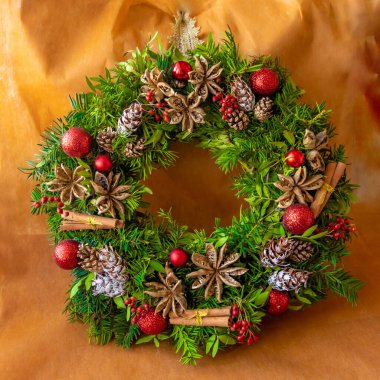 Noel çelengi kozalaklı dallar, kozalaklar, tarçın, turuncu arka planda toplar.