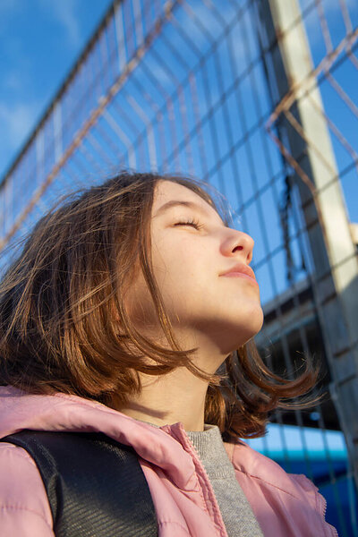Portrait of a beautiful, natural teen girl stretches her face towards the sun on a bright sunny day
