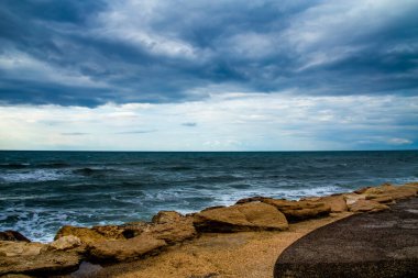 Yağmur ve denizin üzerindeki büyük kara bulutlar, mavi tonların çeşitliliği.