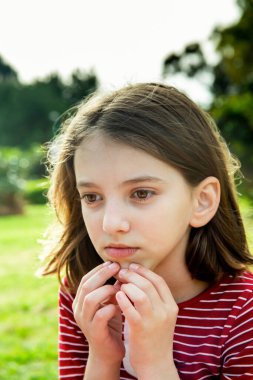 Düşünceli, sevimli, mutlu, kırmızı çizgili tişörtlü, güneşli bir günde yeşil bir kızın portresi.