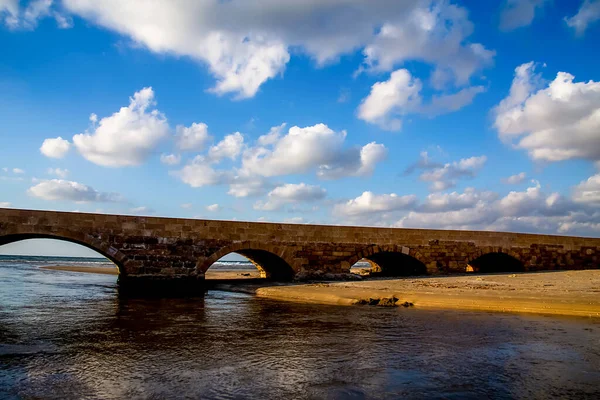 a bridge over a river that flows into the sea or ocean and a blue sky with a lot of white clouds