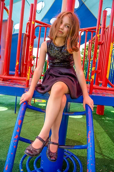 dissatisfied Beautiful emotional natural teenager girl in black dress with sequins sits on the playground