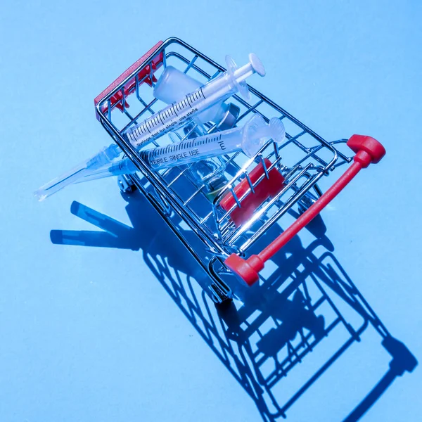 青い背景で買い物のためのミニショッピングトロリーの医療注射器 — ストック写真