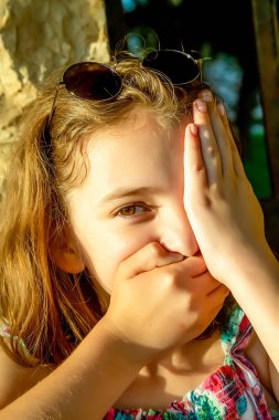 Beautiful emotional natural cute teenager girl covered her mouth with one hand and her eye with the other on a sunny day