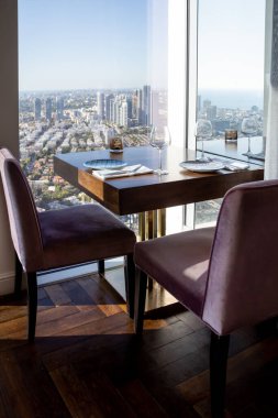 Güneşli bir günde modern şehir binalarına ve denize bakan panoramik pencereli bir lokantada ya da kafede koltuklu masa servis edilir.