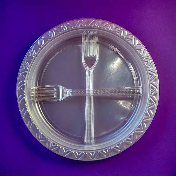 crossed white plastic forks lie on plastic plates. purple background