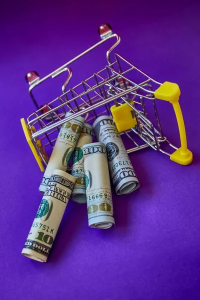 konsept - kıvrımlı dolar banknotları Alışveriş Arabası Tramvayı 'ndan mor arka plana doğru düşüyor