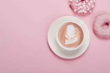 Düz kompozisyon, donutlar ve pembe arka planda bir fincan kahve.