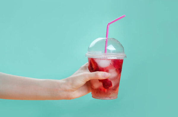 Рука держит стаканы клубничного коктейля на розовом и зеленом фоне
