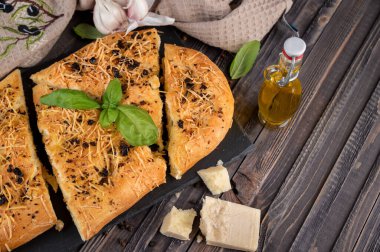 Geleneksel ev yapımı İtalyan düz ekmekleri Focaccia. Sarımsak, parmesan ve fesleğen yapraklı Focaccia, ahşap arka plan, üst manzara 