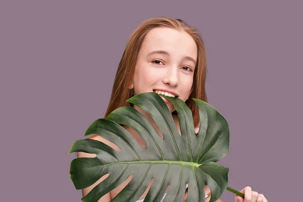 Giovane ragazza sorridente con foglia di monstera. Cosmetologia concetto di salute. — Foto Stock