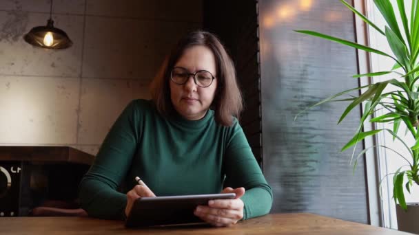 Όμορφη γυναίκα κάθεται στο καφέ και δουλεύει. Πράσινο φόρεμα με μακριά μανίκια — Αρχείο Βίντεο