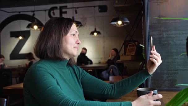 Bonita mujer sentada en la cafetería y hablando. Vestido verde con mangas largas — Vídeos de Stock