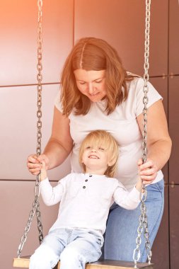 Anne küçük oğlunu salıncakta sallıyor. Açık hava aile portresi. İki kişi birlikte.