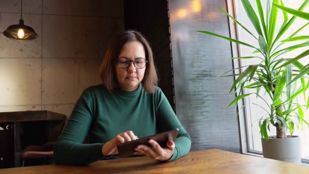 Жінка середнього віку сидить у кафе з планшетом . — стокове відео