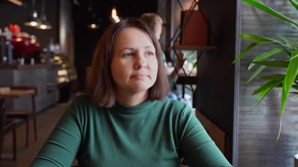 Güzel bir kadın kafede oturuyor ve konuşuyor. Uzun kollu yeşil elbise — Stok video