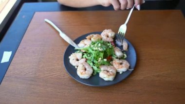 Restoranda karides salatası yiyen genç bir kadın. Sağlıklı gıda konsepti. Çatal, bıçak.