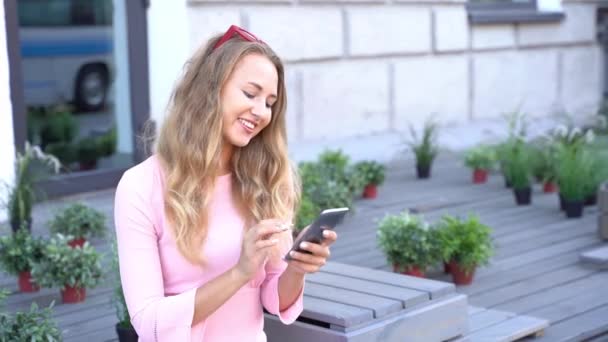 아주 젊은 여성 이 전화로 문자를 하고 있습니다. 야외 카페에 있는 행복 한 여성 — 비디오